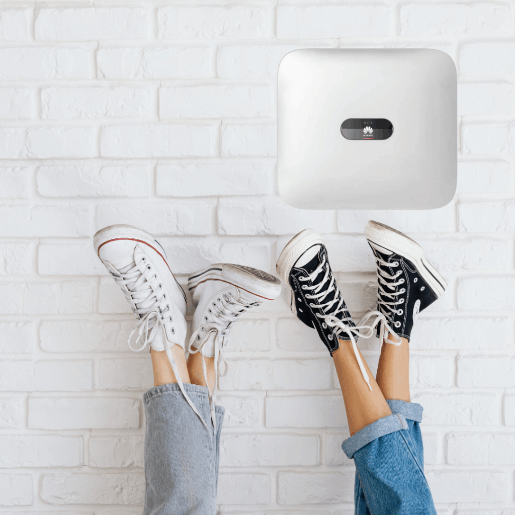 To par ben med converse-sko læner sig op ad en murstensvæg, hvor der hænger en inverter fra huawei